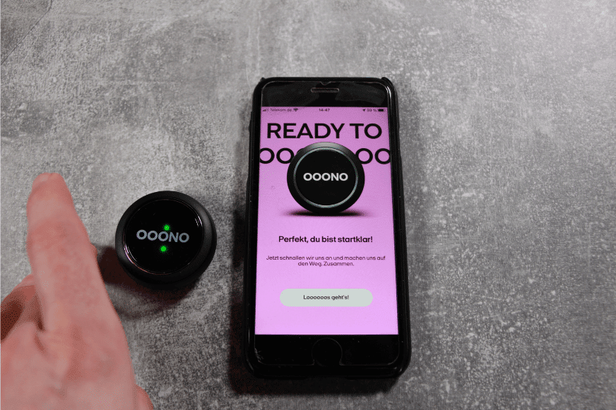 Der Ooono Co-Driver No1 liegt neben dem Smartphone und die App zeigt auf dem Display, dass das Gerät eingerichtet ist